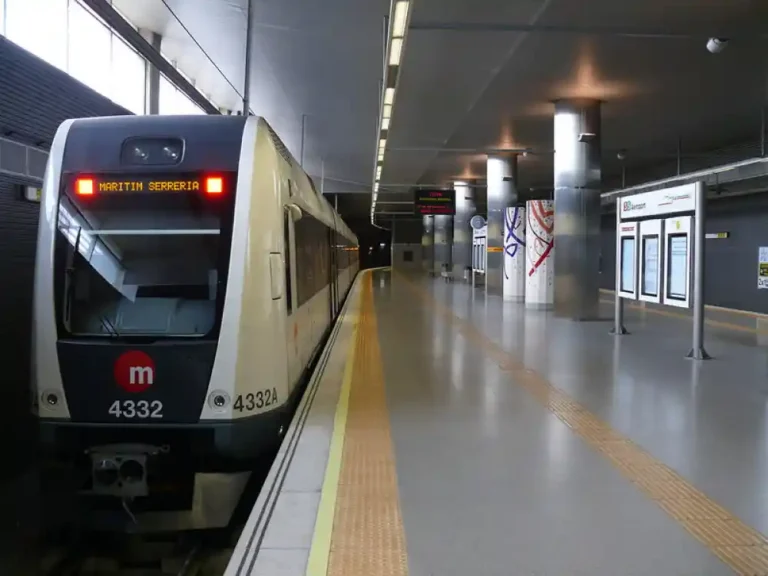 Primer plano de un tren de Metrovalencia de la serie 4300 estacionado en el andén de la estación subterránea Aeroport, con el indicador de destino hacia Marítim Serrería.