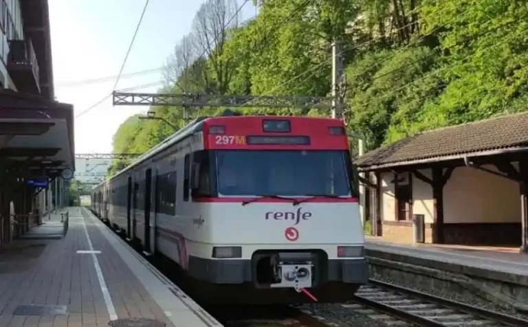Tren de Cercanías Renfe de la serie 447 estacionado en el andén de una estación rodeada de vegetación en el País Vasco.