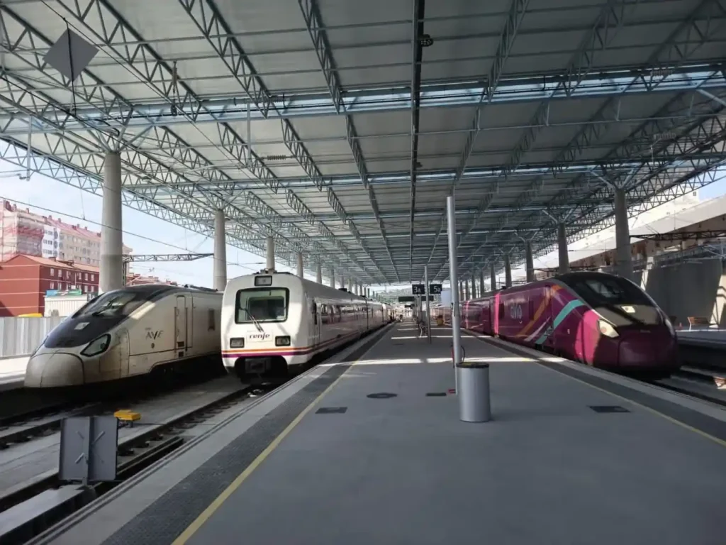 Tres trenes de Renfe, incluidos un AVE y un Avlo, estacionados bajo la gran marquesina metálica y acristalada de la renovada estación intermodal de A Coruña.