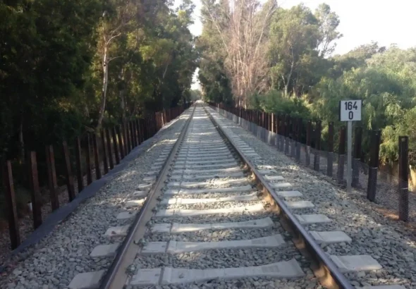 Vista en perspectiva de una vía de tren renovada con traviesas de hormigón y balasto, flanqueada por vegetación y una señalización con el punto kilométrico 164