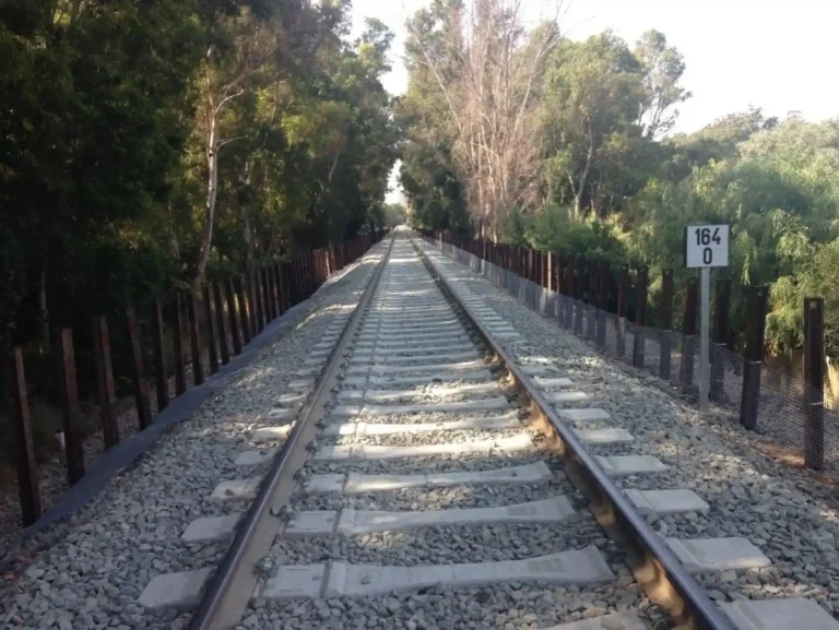 Vista en perspectiva de una vía de tren renovada con traviesas de hormigón y balasto, flanqueada por vegetación y una señalización con el punto kilométrico 164
