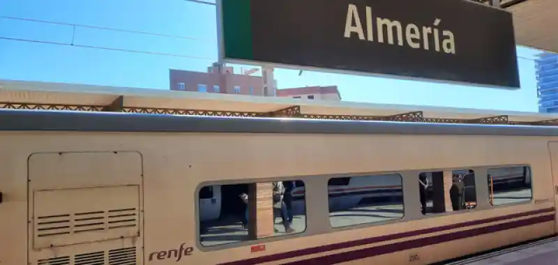 Vagón de un tren Talgo de Renfe estacionado en la estación de tren de Almería, debajo del cartel identificativo de la estación.