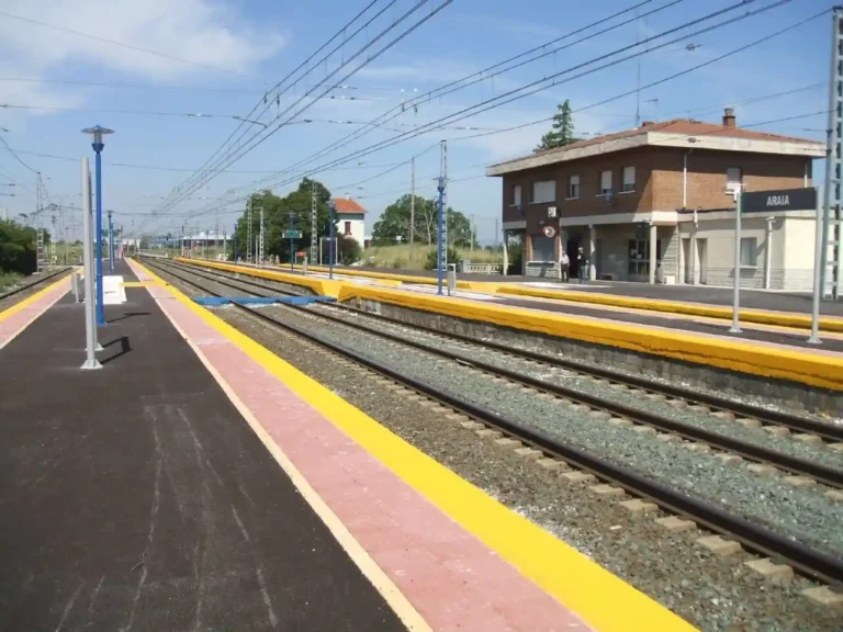 Vías del tren y andenes de la estación de ferrocarril de Araia, con el edificio principal de ladrillo a la derecha y catenarias sobre las vías.