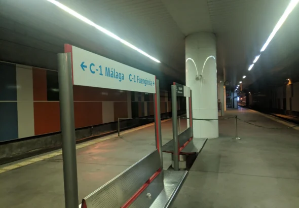 Andén subterráneo de la estación de Victoria Kent con bancos metálicos y un cartel indicador de la línea C-1 hacia Málaga y Fuengirola, bajo una hilera de luces de techo encendidas.