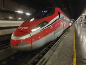 Primer plano de un tren de alta velocidad Iryo de color rojo y plateado, estacionado en el andén de una estación ferroviaria.