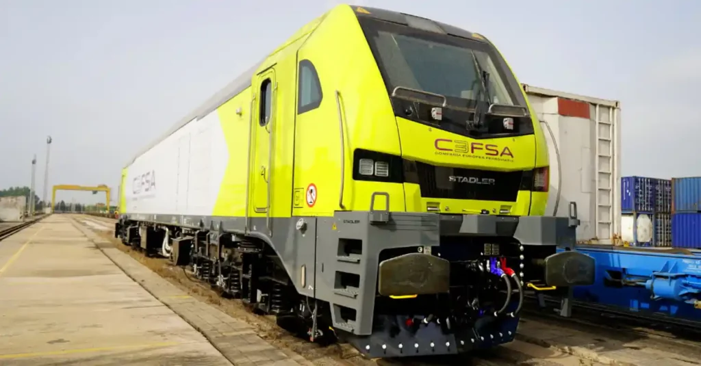 Vista frontal de una locomotora eléctrica Stadler Euro 6000 de color amarillo fluorescente y gris con el logotipo de CEFSA en una vía de carga.