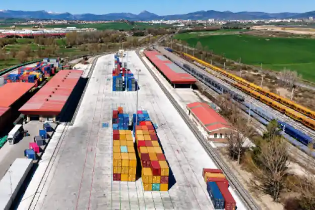 Vista aérea de la renovada terminal logística de Noaín con contenedores intermodales de varios colores ordenados en la explanada de hormigón y vías de tren a los lados.