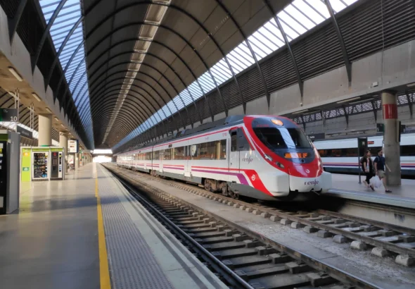 Un tren de Renfe Cercanías estacionado en la vía de la estación de Sevilla-Santa Justa bajo su característica cubierta abovedada de acero y cristal.