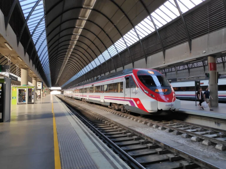 Un tren de Renfe Cercanías estacionado en la vía de la estación de Sevilla-Santa Justa bajo su característica cubierta abovedada de acero y cristal.