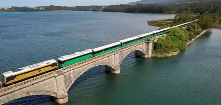 Vista aérea del tren turístico Costa Verde Express cruzando un viaducto sobre un estuario rodeado de vegetación, durante las pruebas con combustible 100% renovable HVO.Vista aérea del tren turístico Costa Verde Express cruzando un viaducto sobre un estuario rodeado de vegetación, durante las pruebas con combustible 100% renovable HVO.