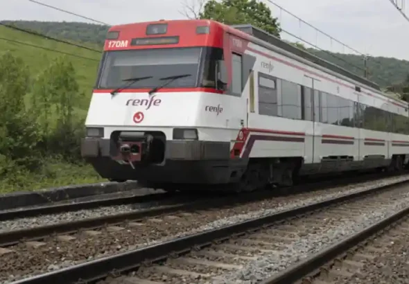Un tren de Cercanías Renfe de color blanco y rojo circula por una vía de tren rodeada de prados verdes y colinas en el territorio de Gipuzkoa, dirección andonain.