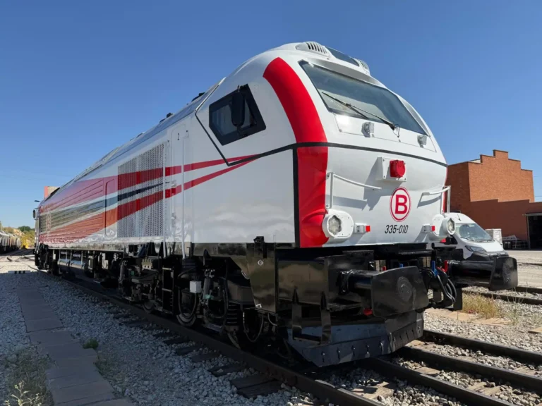 Locomotora diésel-eléctrica de mercancías modelo Euro 4000 (matrícula 335-010) de color blanco con franjas rojas y negras, estacionada sobre las vías en un día despejado.