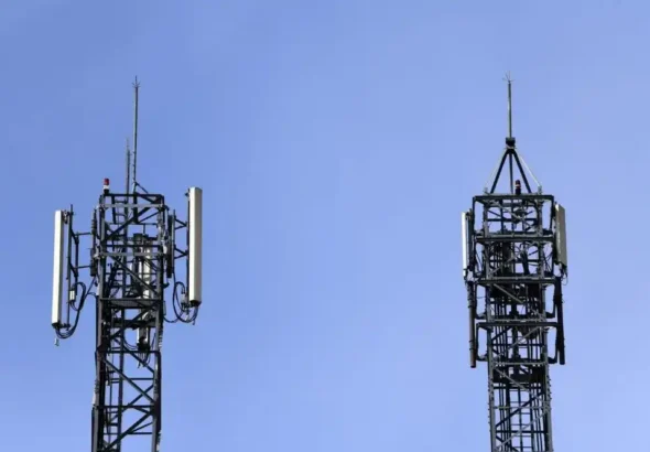 Dos torres metálicas con antenas y paneles de telecomunicaciones instaladas en la línea de trenes de alta velocidad entre Atocha y Torrejón, bajo un cielo azul claro.
