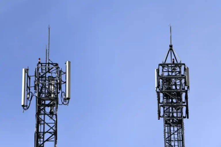 Dos torres metálicas con antenas y paneles de telecomunicaciones instaladas en la línea de trenes de alta velocidad entre Atocha y Torrejón, bajo un cielo azul claro.
