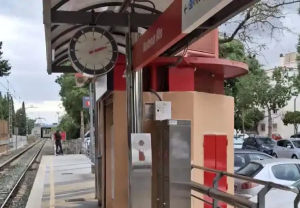 Vista del andén y la vía única en la estación de tren de Cercanías Montemar Alto, con el letrero identificativo rojo, el reloj de la estación y turismos estacionados al fondo.