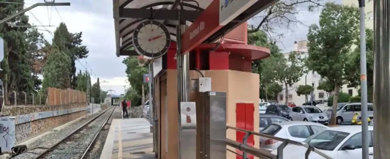 Vista del andén y la vía única en la estación de tren de Cercanías Montemar Alto, con el letrero identificativo rojo, el reloj de la estación y turismos estacionados al fondo.