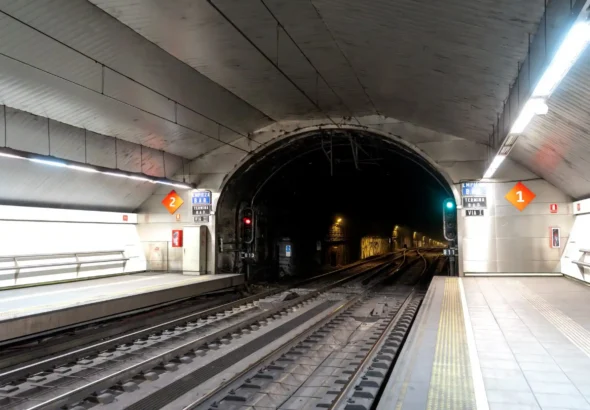 Vista subterránea de los andenes y las vías del tren en la estación de Cercanías de Laguna, con la boca de un túnel al fondo y señales ferroviarias iluminadas.