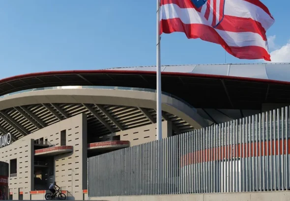 Exterior del Estadio Metropolitano en Madrid con la bandera del Atlético de Madrid y las inmediaciones de la estación de Metro Estadio Metropolitano en un día soleado.