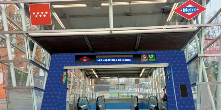 Entrada a la estación de Metro de Madrid con estructura de cristal, señalizada con el nombre 'Los Espartales-Coliseum' sobre vinilo azul con patrones y los logotipos institucionales y de Metro. Foto modificada.
