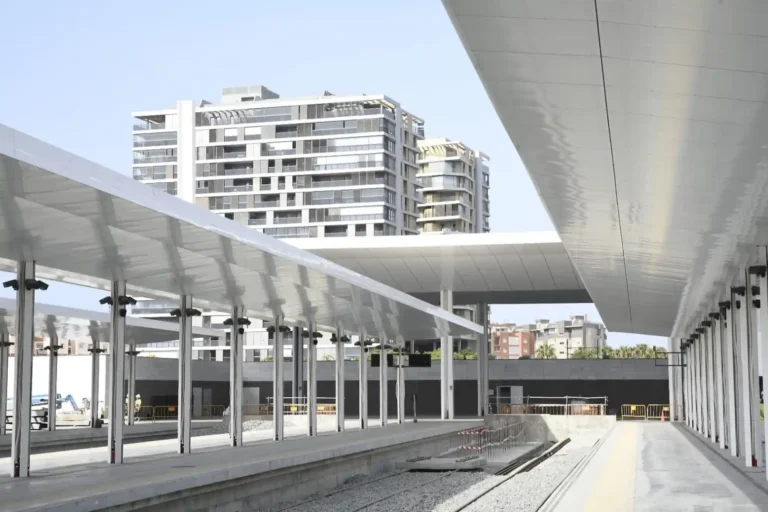 Vista de los andenes y cubiertas metálicas en construcción de la nueva estación intermodal de Almería, con las vías ferroviarias al descubierto y modernos edificios residenciales al fondo.
