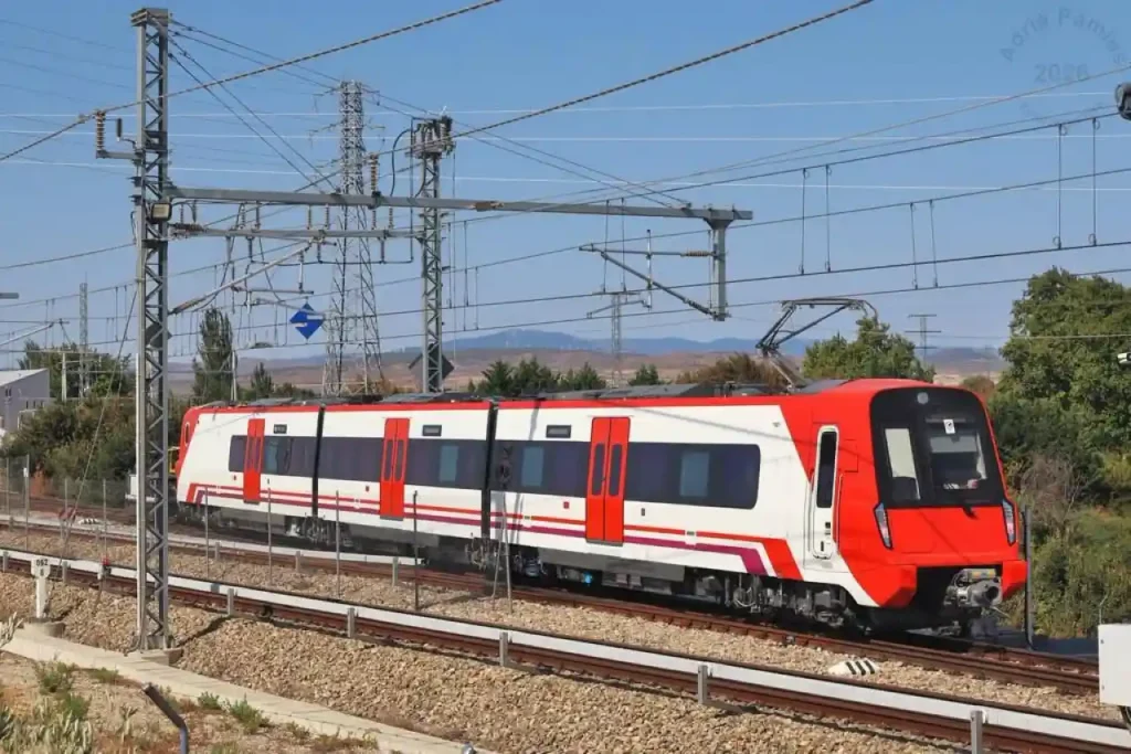 Tren de cercanías blanco y rojo de la Serie 413 circulando por una vía electrificada al aire libre durante una jornada de pruebas.