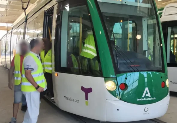 Un convoy del Tranvía de Jaén blanco y verde estacionado en el taller de Vaciacostales mientras varios operarios y formadores con chalecos reflectantes de alta visibilidad suben al vehículo para iniciar las pruebas de maniobra.