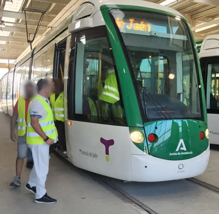 Un convoy del Tranvía de Jaén blanco y verde estacionado en el taller de Vaciacostales mientras varios operarios y formadores con chalecos reflectantes de alta visibilidad suben al vehículo para iniciar las pruebas de maniobra.
