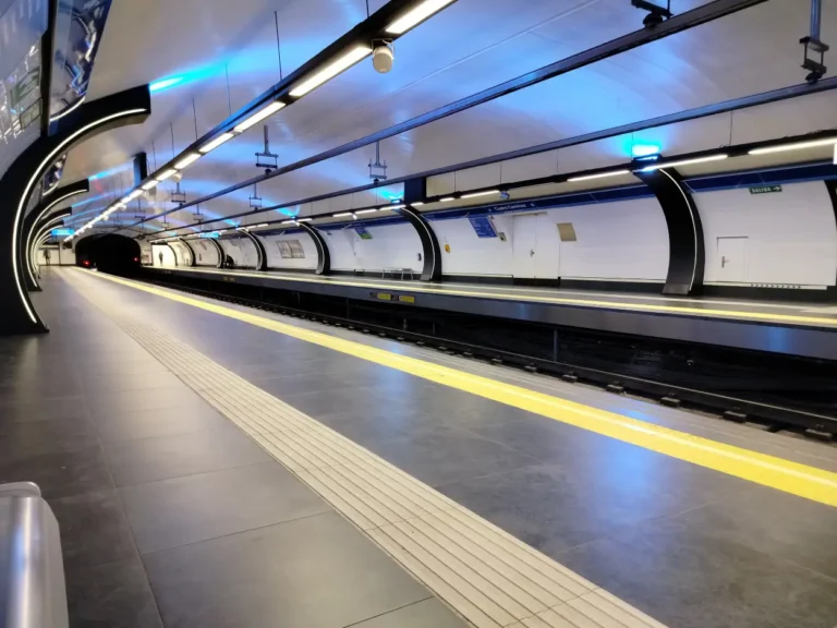 Vista en perspectiva del andén de una estación subterránea de Metro de Madrid, iluminada con luces LED y arcos metálicos decorativos en la bóveda.