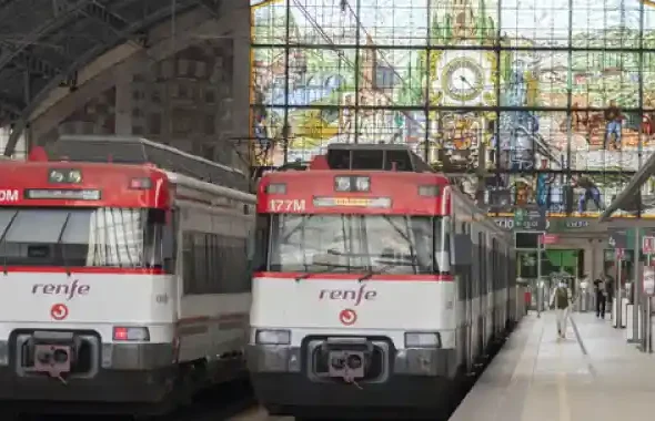 Dos trenes de Renfe Cercanías estacionados en los andenes de la estación de Bilbao Abando, frente a la gran vidriera histórica del fondo.