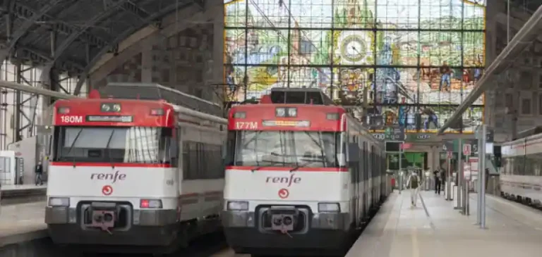 Dos trenes de Renfe Cercanías estacionados en los andenes de la estación de Bilbao Abando, frente a la gran vidriera histórica del fondo.