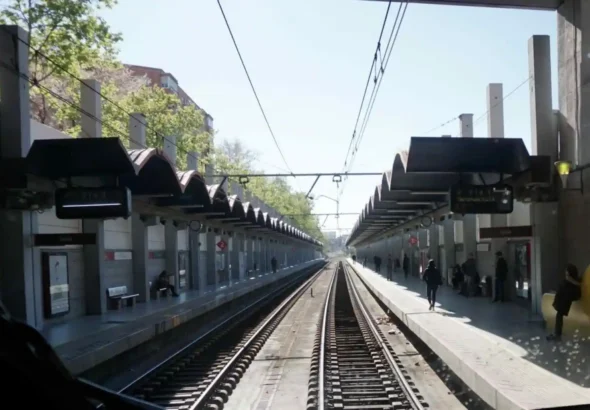 Perspectiva desde la cabina de un tren que muestra las vías centrales, la catenaria aérea y los dos andenes laterales con marquesinas de la estación de tren de Delicias en Madrid.