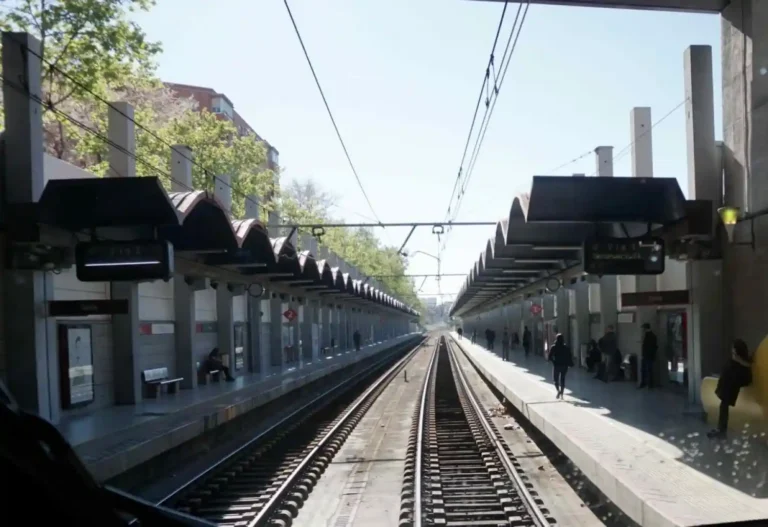 Perspectiva desde la cabina de un tren que muestra las vías centrales, la catenaria aérea y los dos andenes laterales con marquesinas de la estación de tren de Delicias en Madrid.