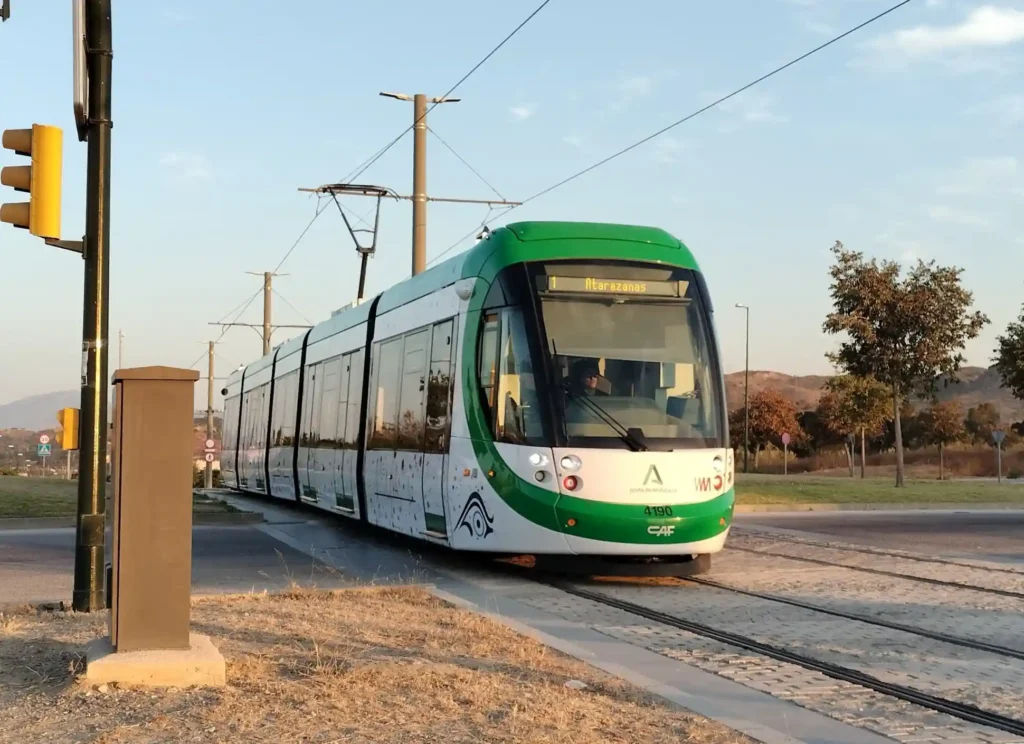 Unidad moderna de tranvía del Metro de Málaga, de colores blanco y verde, circulando por la vía al aire libre con el letrero luminoso superior marcando la Línea 1 hacia Atarazanas.