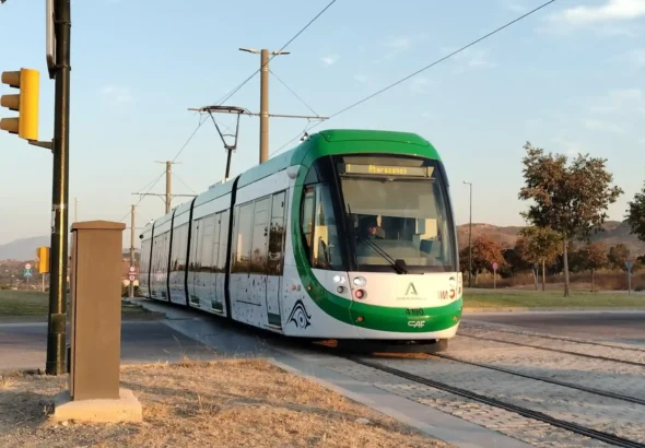 Unidad moderna de tranvía del Metro de Málaga, de colores blanco y verde, circulando por la vía al aire libre con el letrero luminoso superior marcando la Línea 1 hacia Atarazanas.