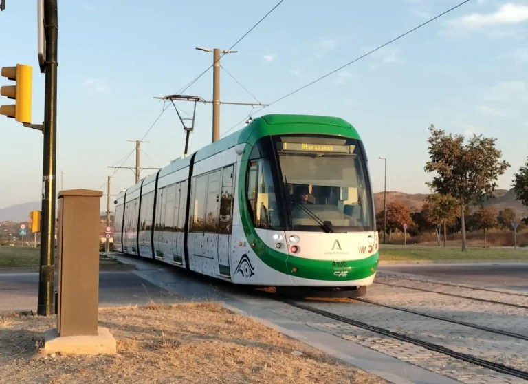 Unidad moderna de tranvía del Metro de Málaga, de colores blanco y verde, circulando por la vía al aire libre con el letrero luminoso superior marcando la Línea 1 hacia Atarazanas.