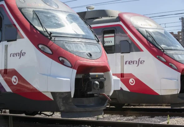 Primer plano de la parte frontal de dos trenes Civia de Cercanías Renfe de colores blanco, rojo y morado, estacionados en las vías de la estación.