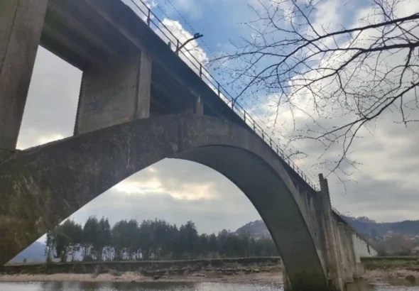 Vista inferior de un viaducto ferroviario de hormigón con un gran arco central sobre el río Nalón en Asturias, rodeado de vegetación y bajo un cielo parcialmente nublado.
