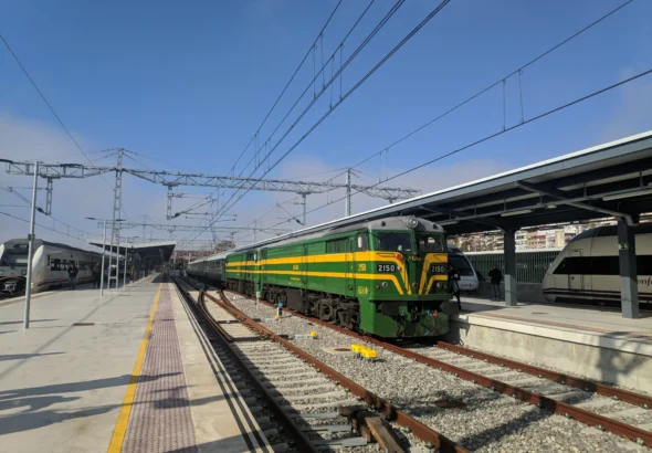 Locomotora diésel clásica de la serie 321/ALCo en tonos verde y amarillo de ALSA, estacionada en una vía de estación junto a sus coches de viajeros de los años 60.