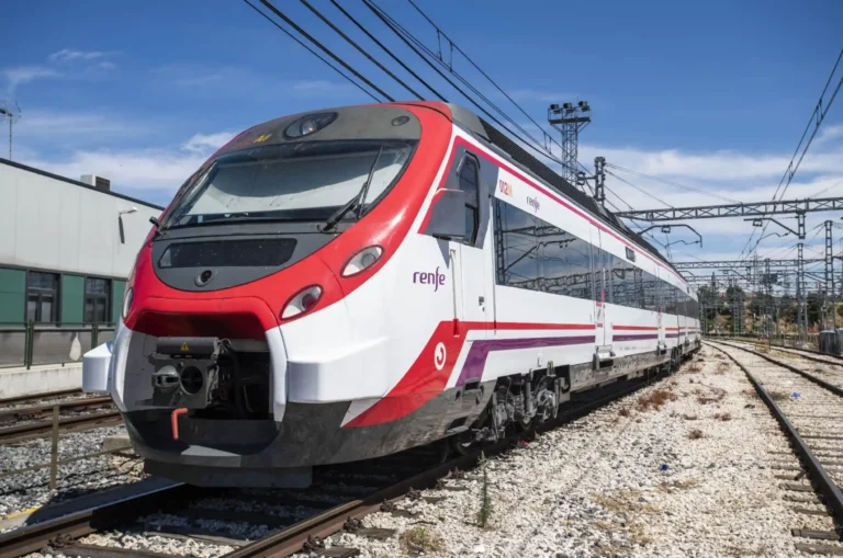 Tren Civia de Cercanías Renfe de colores blanco, rojo y morado estacionado sobre las vías de la red ferroviaria bajo un cielo despejado. los cortes en el túnel de sol son para realizar un nuevo esquema de vías.