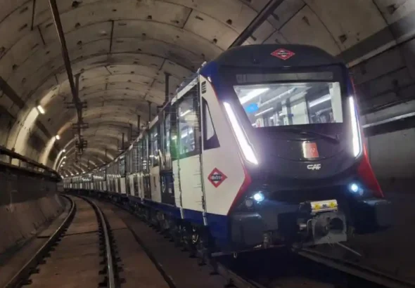 Tren moderno de Metro de Madrid de la marca CAF, con los colores blanco, azul y rojo, circulando dentro de un túnel subterráneo iluminado.